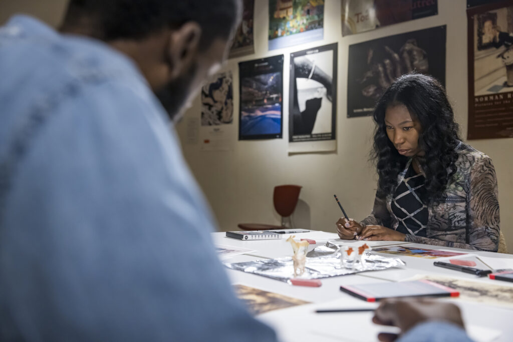 A woman concentrates while sketching three toy animals in front of her.