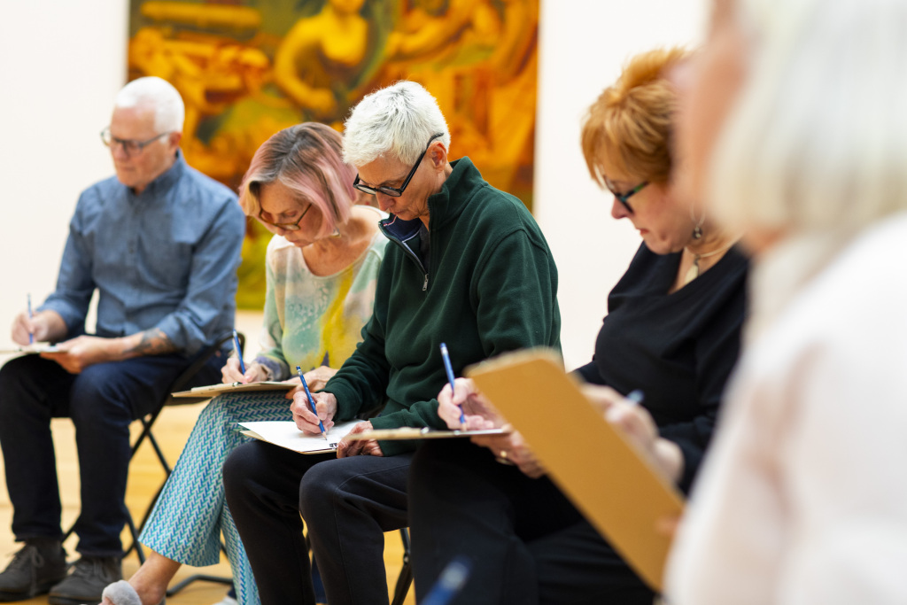 A group of individuals drawing while sitting in a gallery.